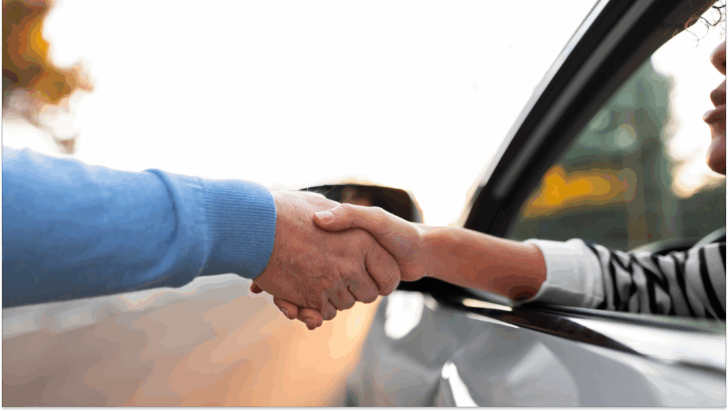 Homem dentro do carro aperta a mão do homem fora do carro, para falar sobre transferir a proteção veicular