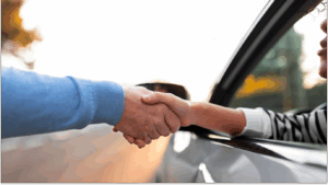 Homem dentro do carro aperta a mão do homem fora do carro, para falar sobre transferir a proteção veicular
